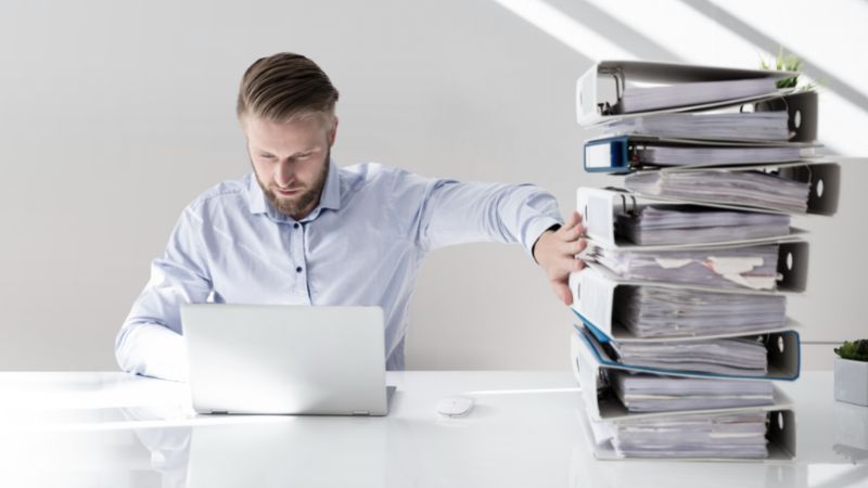 Herr vor Laptop mit Stapel von Papier-Ordnern